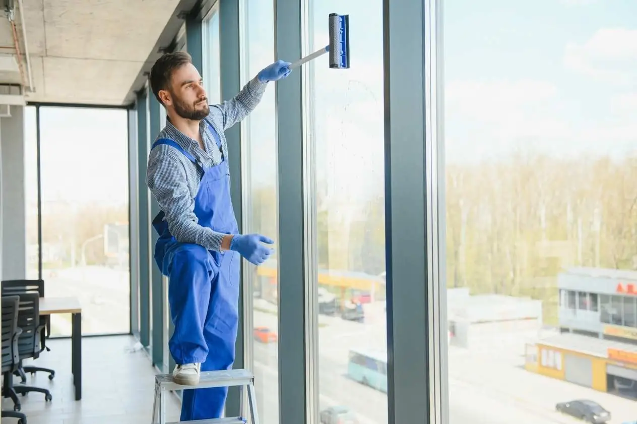 Window cleaner on a step stool cleaning floor-to-ceiling office windows from the inside